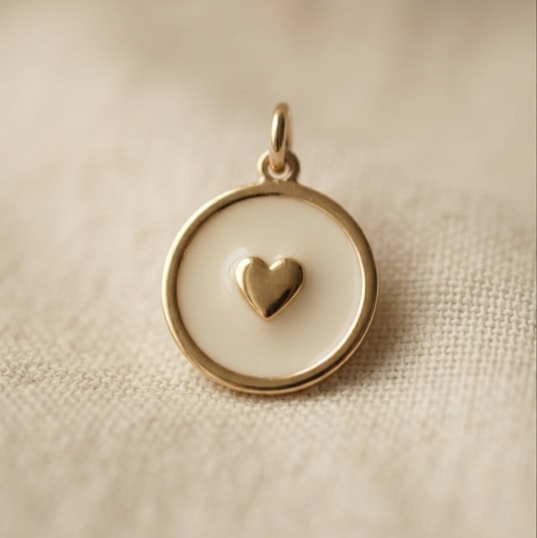 A small round gold pendant with a white center and a tiny gold heart in the middle